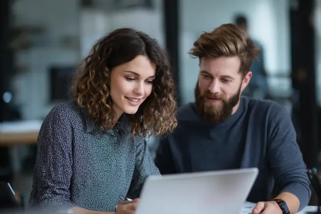 mann und frau sitzen beide am Tisch hinter einem Laptop Bildschirm